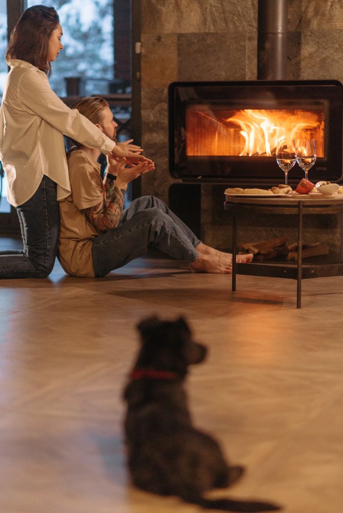 A couple enjoying warmth by the fireplace with their dog at home.